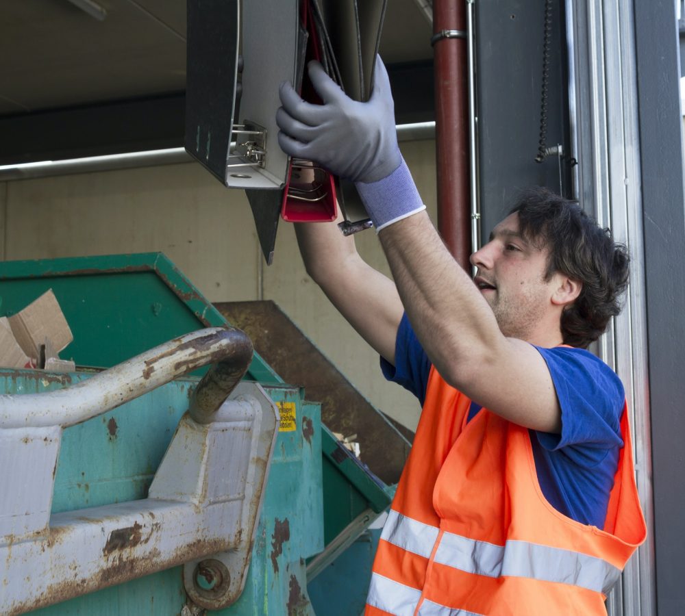 Worker At A Waste Container Throwing Away Folders.jpg